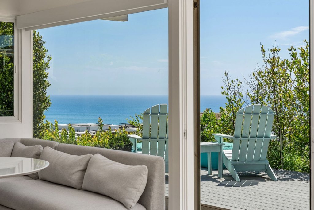 Coastal living room opening to a deck with two Adirondack chairs overlooking the Pacific