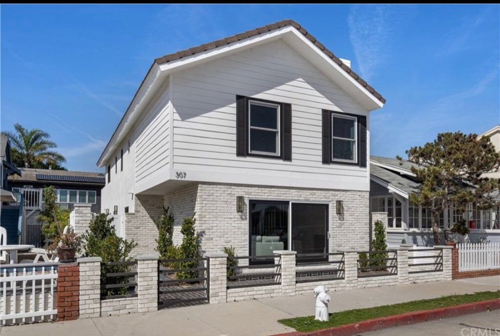 White two-story beach cottage with brick base and black shutters