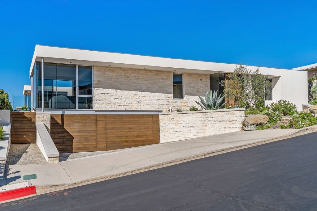 Single-story modern home with limestone walls, glass corner and cedar garage doors
