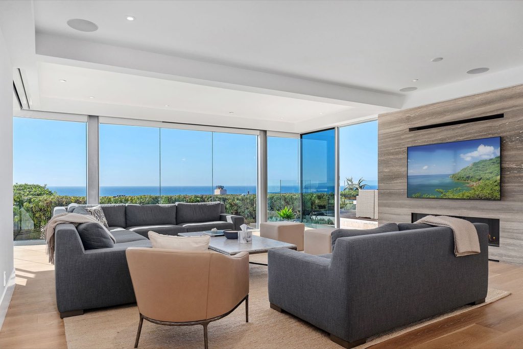 Ocean-view living room with floor-to-ceiling glass and a travertine fireplace wall